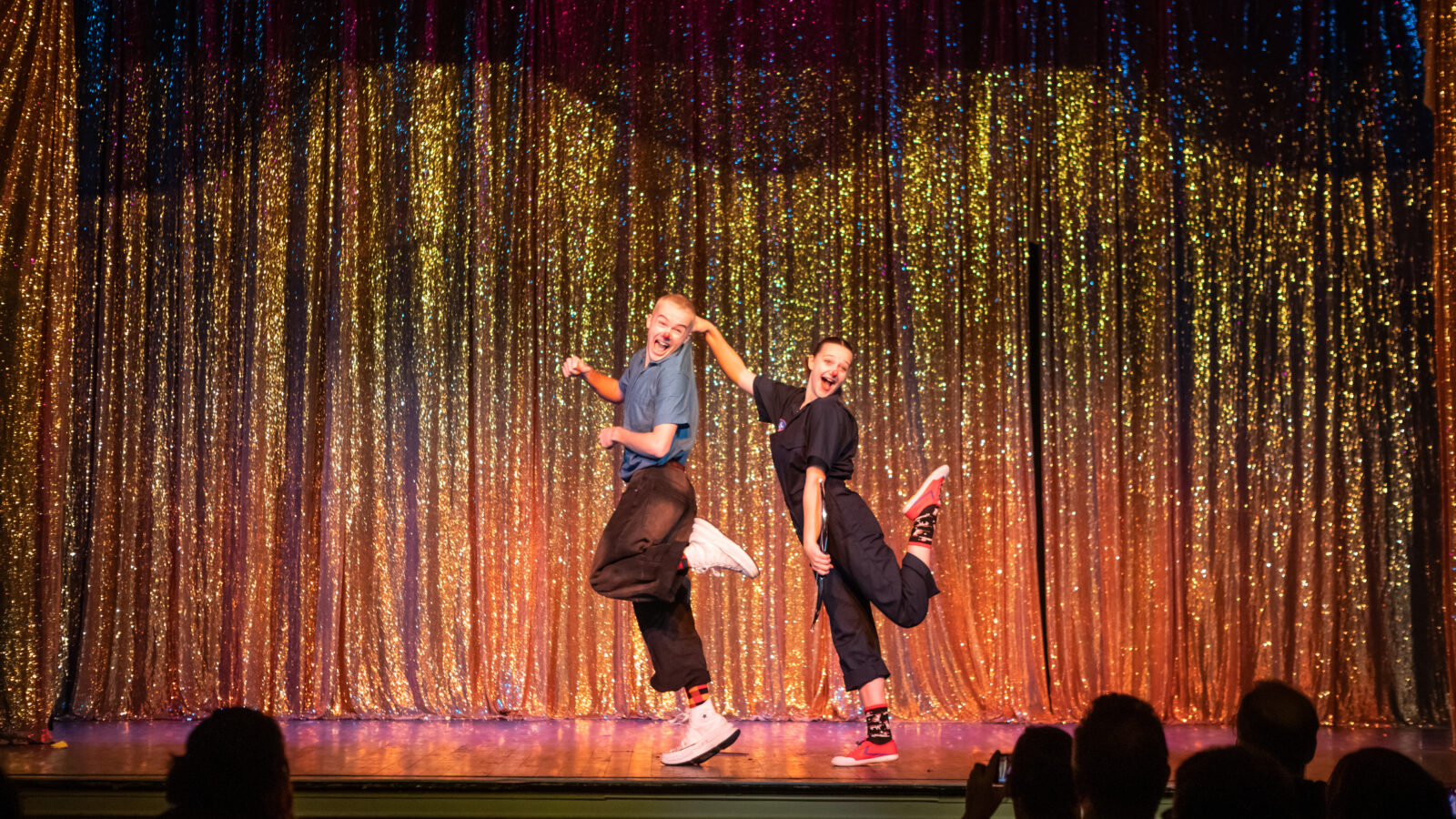 a photograph of Circus Smirkus performing at Highlight New Year's Eve. A light skinned young ma and woman dance in unison on a stage with a sparkly copper colored curtain behind them