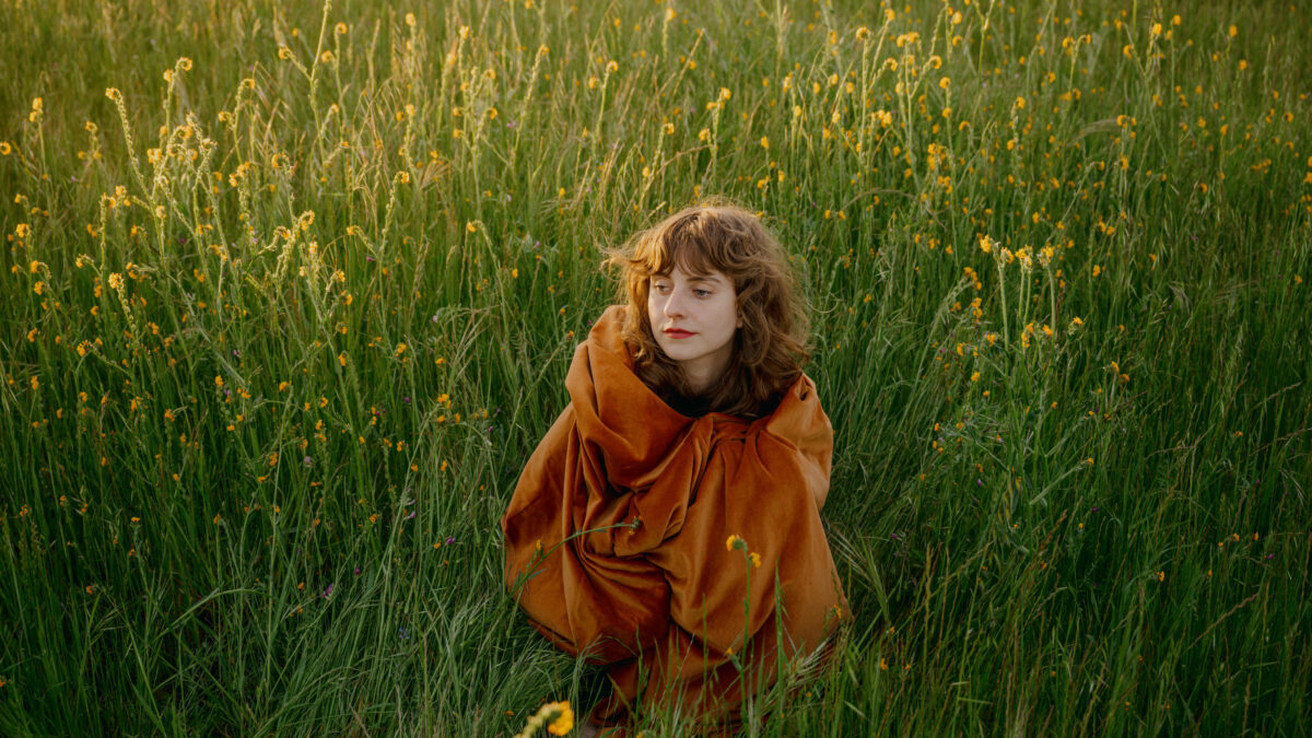 A photo of Hannah Francis standing in a field of tall grass and wild flowers