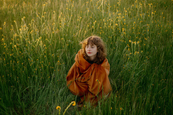 A photo of Hannah Francis standing in a field of tall grass and wild flowers